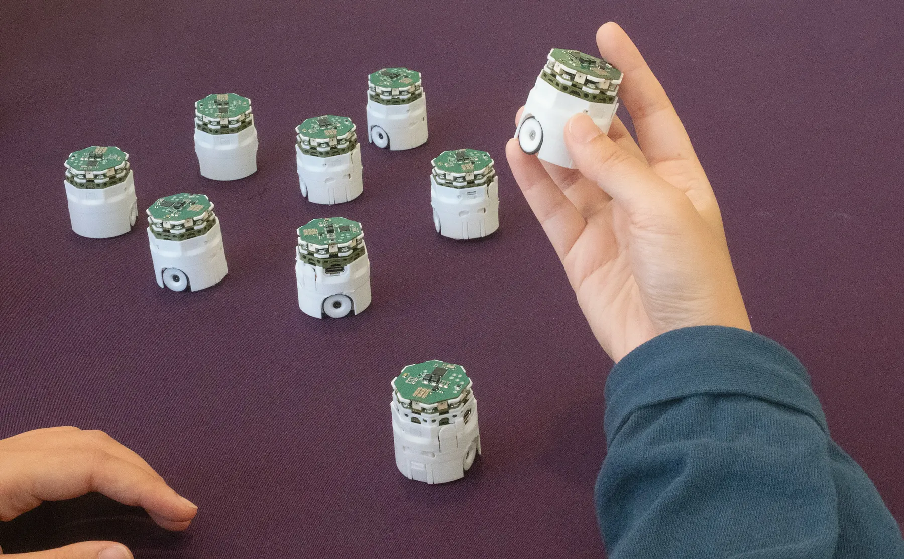 A hand holding one robot above others on a purple table.