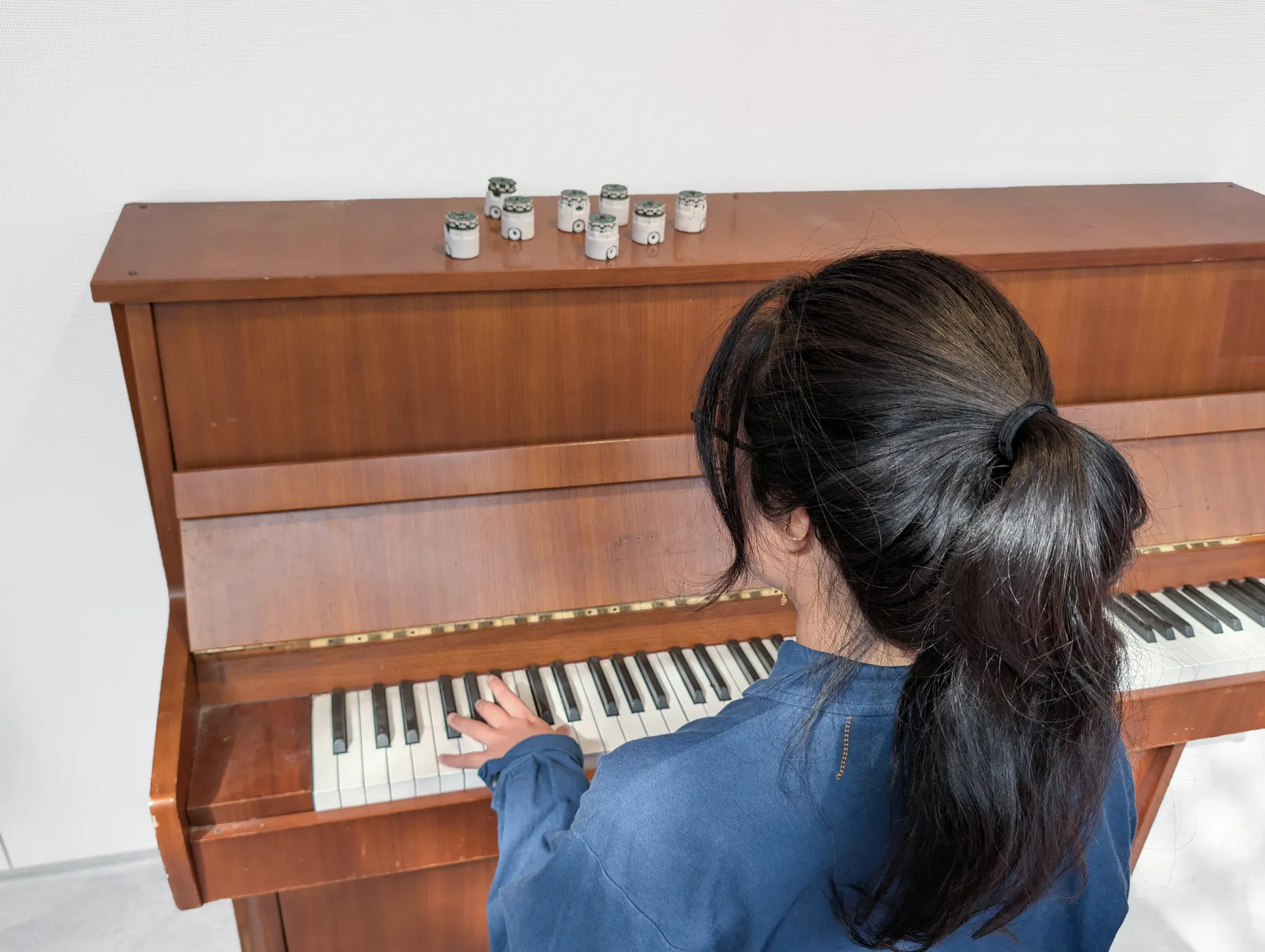 A pianist playing an upright piano with robots standing on top of it.