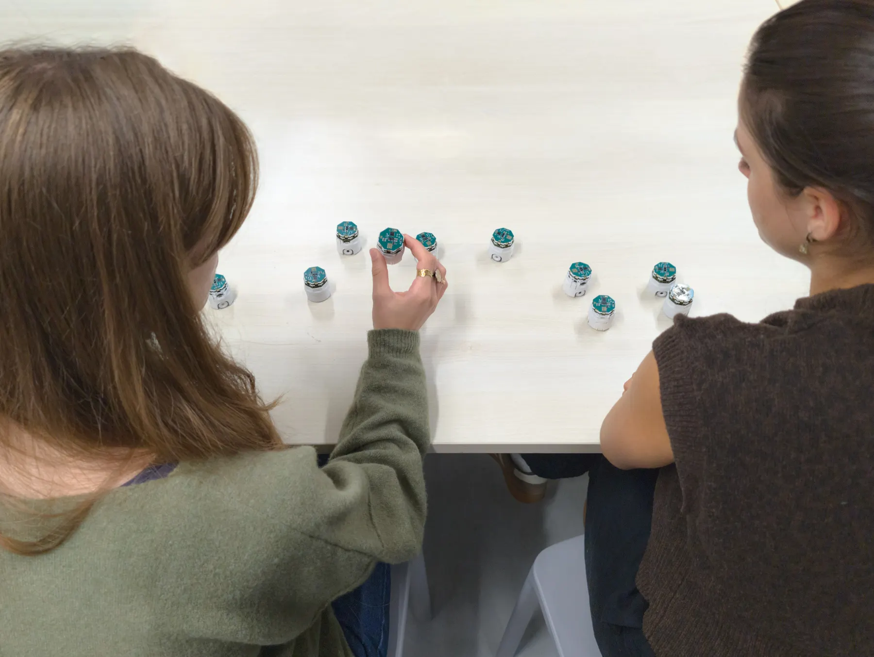 Two students at a table, one placing a robot among others.
